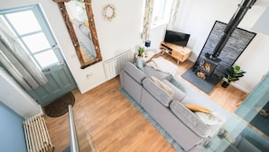 A modern living room with a grey sofa, a wooden TV stand, a fireplace, and a large mirror. - Bramble Cottage a stunning detached cottage in the heart of St Columb Minor. (Newquay)