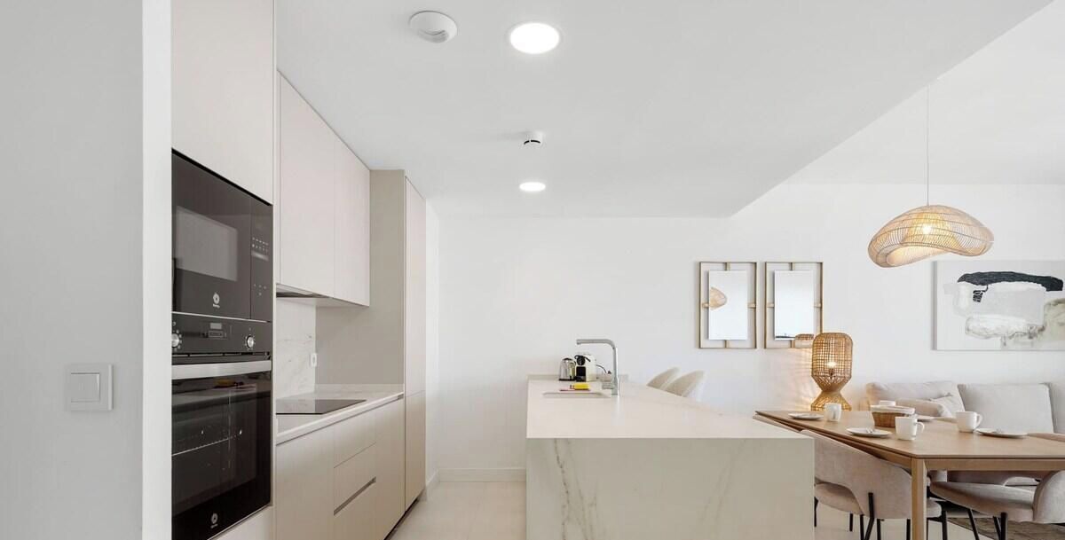 Una cocina moderna con electrodomésticos integrados, un comedor con una isla de mármol e iluminación colgante.