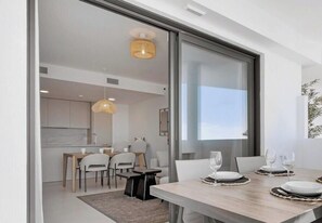 A modern dining area with a table set for four, a kitchen in the background, and a large window providing natural light.