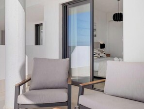 A modern room with two grey armchairs, a large sliding glass door leading to a balcony, and a hanging pendant light.