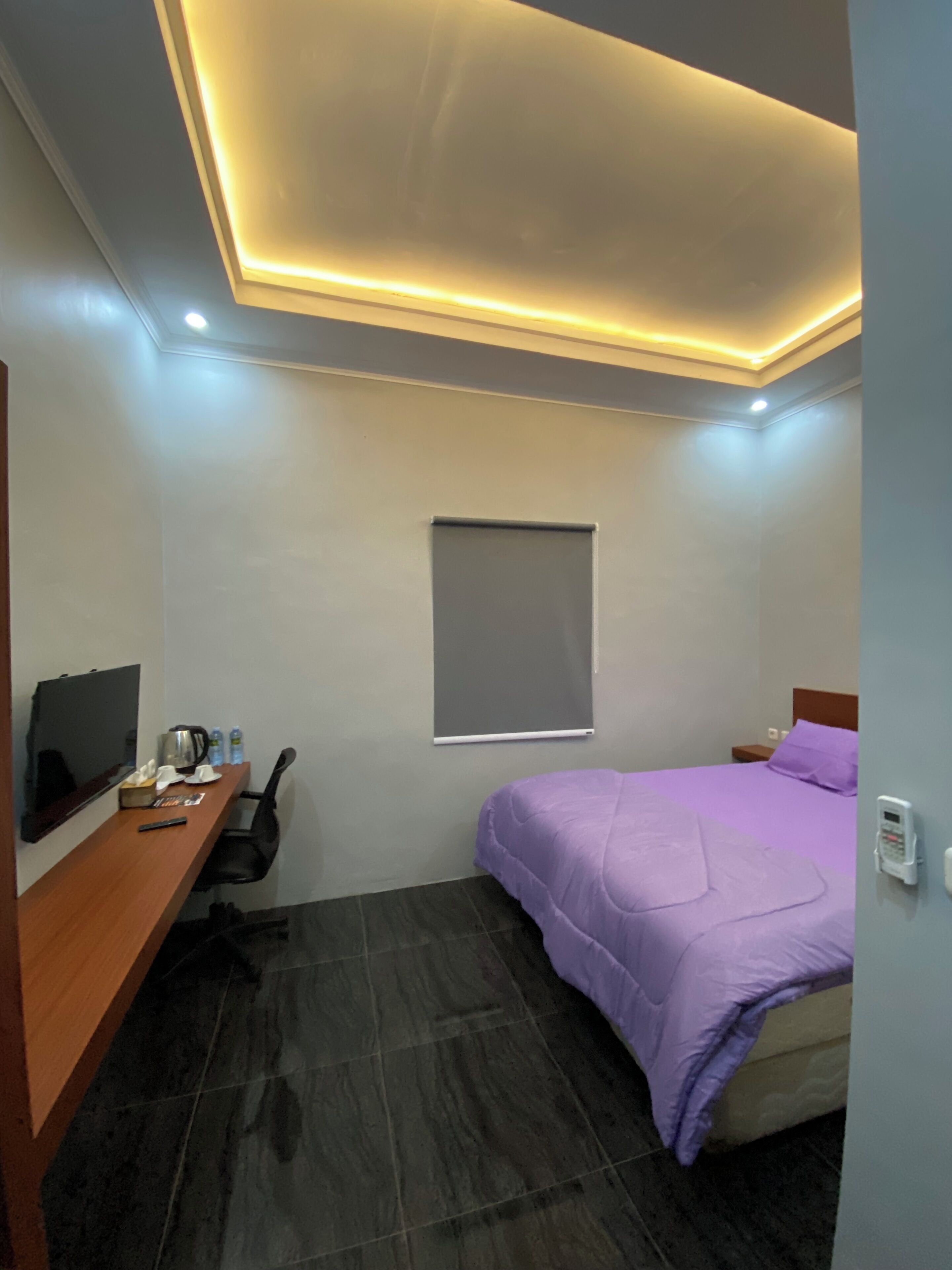 A bedroom with a bed, a TV, a desk, and a window.