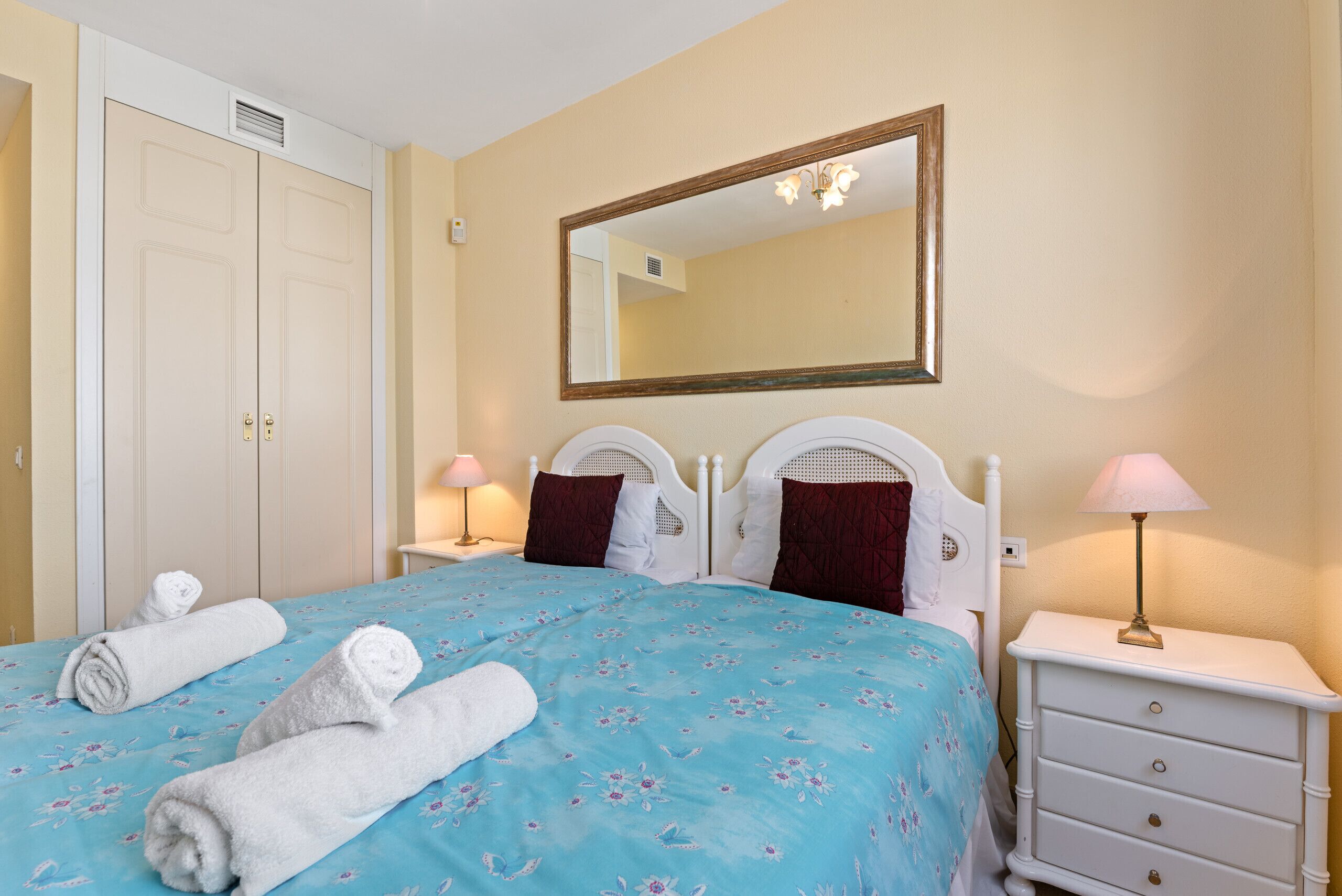 A bedroom with a bed, two bedside tables, a nightstand, a mirror, and a wardrobe.