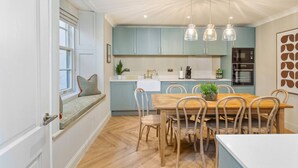 Une cuisine moderne avec des meubles de couleur bleu clair, une table à manger en bois avec des chaises et des luminaires suspendus.