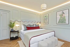 Une chambre à coucher bien rangée, avec un lit, des lampes de chevet, une table de nuit, une plante en pot et des œuvres d’art accrochées aux murs.