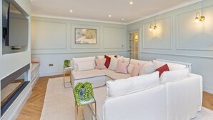 Un salon moderne avec un canapé d’angle, un téléviseur à écran plat fixé au mur et une petite table d’appoint agrémentée d’une plante.