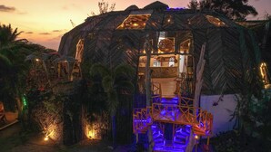 A thatched-roof structure with a staircase leading to an entrance, surrounded by greenery. - Samay Playas (Playas)