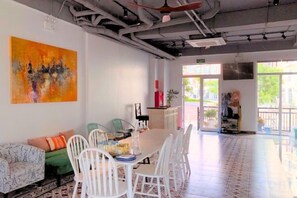 A spacious room with a dining table, chairs, and a sofa. There is a large window providing natural light and a view of the outdoors. - Moonlight Hotel Phu Quoc (Phu Quoc Island)
