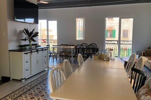 A dining area with a long table, chairs, and a kitchen area with cabinets and a plant. - Moonlight Hotel Phu Quoc (Phu Quoc Island)