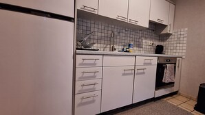 Una cocina compacta con armarios blancos, salpicadero de azulejos, horno empotrado y un pequeño cubo de basura.