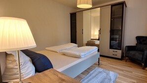 Un dormitorio con cama, lámpara de noche, armario y una silla.