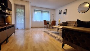 Una sala de estar con sofá, televisor, piso de madera y un comedor con sillas y mesa.