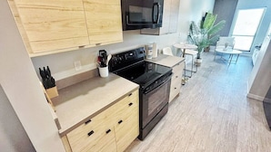 A modern kitchen with wooden cabinets, a black microwave, a stove, and a small dining area with a table and chairs.