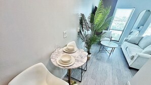 A modern living room with a round table set for four, a white sofa, and a large potted plant.