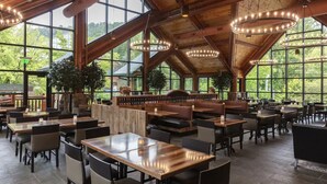 Un vaste espace intérieur aménagé en salle à manger, avec de hauts plafonds, de grandes fenêtres, ainsi que des tables et des chaises en bois.