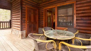 Une cabane en rondins avec une façade en bois, une porte en verre, des meubles en osier et une terrasse en bois.