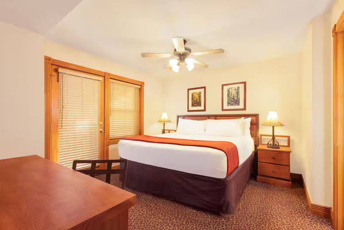 Ein Hotelzimmer mit einem Bett, zwei Nachttischlampen, einem Deckenventilator, einem Holztisch und einem Stuhl.