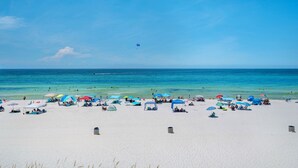 Ein Strand mit weißem Sand, klarem blauen Wasser und mehreren bunten Sonnenschirmen.