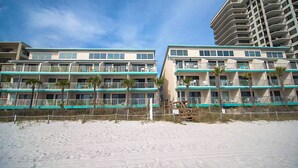 Ein Hotel direkt am Strand mit mehreren Balkonen, einem Sandstrand davor und blauem Himmel.