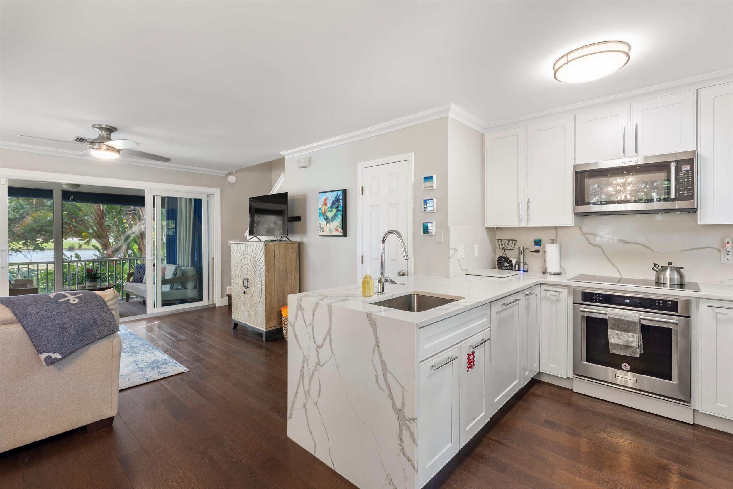 A modern kitchen with white cabinetry, a marble island, stainless steel appliances, and a sliding glass door leading to a balcony.