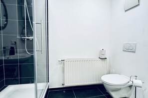 Une salle de bain avec une douche à parois de verre, des toilettes blanches, un radiateur blanc et un lavabo blanc.