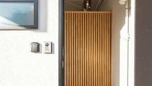 Une porte en bois à lattes, un interphone fixé au mur et une petite marche menant à une pièce.