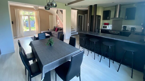 Une cuisine moderne dotée d’un îlot central, d’un coin repas avec une table et des chaises, et d’un espace de vie avec un canapé.