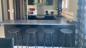 Une cuisine moderne dotée d’un îlot central, de tabourets noirs, d’appareils électroménagers en acier inoxydable et d’un rideau à motifs.