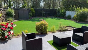 Une terrasse dotée de meubles en osier, une pelouse bien entretenue et une clôture en bois.