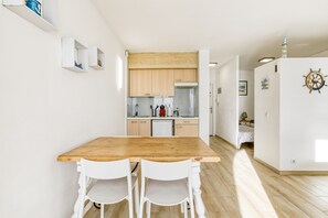 A modern kitchen with wooden cabinets, a stainless steel refrigerator, and a dining area with a wooden table and white chairs.