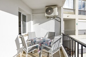 A balcony with a table and chairs, an air conditioning unit, and a building with balconies and windows.