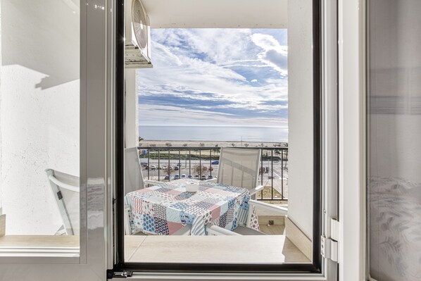 A balcony with a table, chairs, and a view of the sea and parking lot.