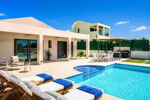 Ein moderner Poolbereich mit Liegestühlen, einem Schwimmbecken und einer überdachten Terrasse.