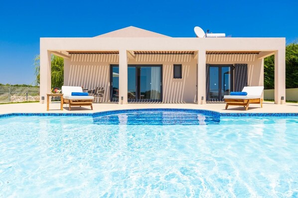 Un área moderna junto a la piscina con dos sillas reclinables y una piscina de color azul claro.