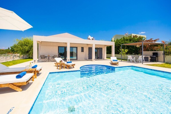 A modern outdoor swimming pool area with lounge chairs and a covered seating area.