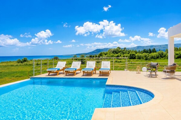 A pool with lounge chairs and a view of the sea.