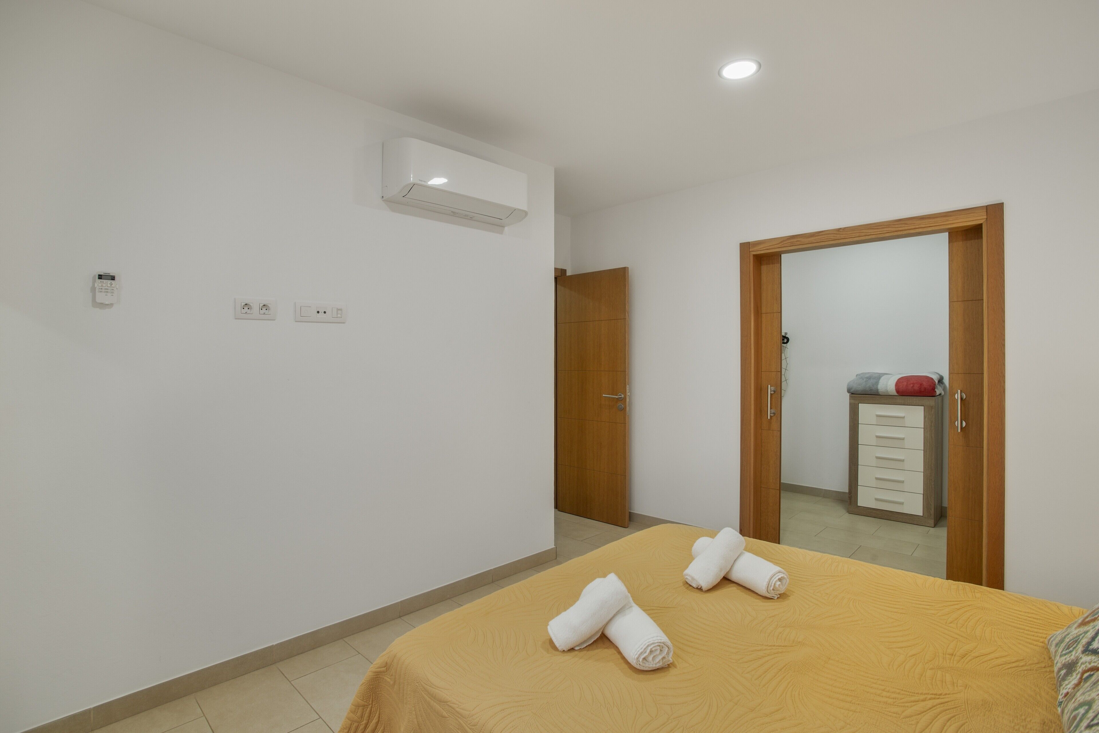 A hotel room with a bed, a wooden wardrobe, a mirror, and an air conditioning unit.