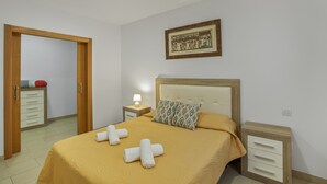 A neatly arranged bedroom with a bed, bedside tables, a nightstand, and a door leading to another room.