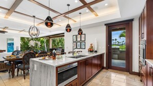 A modern kitchen with a large island, wooden cabinets, and pendant lighting. - Laule‘a #13 by Gather – Mauna Lani 4BR Villa w/ Golf Frontage, Private Pool/Spa (Kamuela)