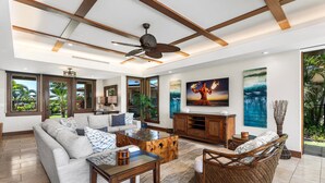 A spacious living room with a sofa, coffee table, and wicker chair. There is a television on the wall and a ceiling fan. - Laule‘a #13 by Gather – Mauna Lani 4BR Villa w/ Golf Frontage, Private Pool/Spa (Kamuela)