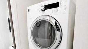 Eine übereinander gestapelte Waschmaschine und Trockner in einem Badezimmer mit Toilette und einer schwarzen Matte.