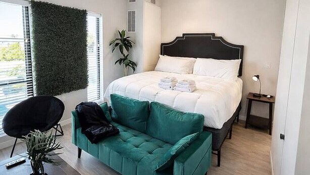 Ein Schlafzimmer mit einem Bett, einem grünen Sofa, einem kleinen Tisch und einer Topfpflanze.
