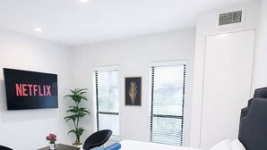 A modern hotel room with a large bed, a desk, a chair, a TV, and a potted plant. - Modern East Village Studio | Stylish Comfort near Dining & Shops (Des Moines)
