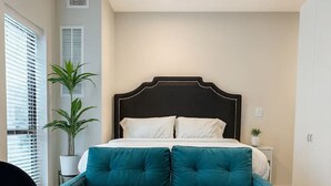 A room with a bed, a teal sofa, a coffee table with a vase of red flowers, and a black chair. - Modern East Village Studio | Stylish Comfort near Dining & Shops (Des Moines)