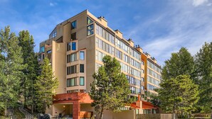 Ein mehrstöckiges Hotel mit modernem Design, das einen zentralen Eingangsbereich mit Überdachung und einen Parkplatz vor dem Gebäude bietet.