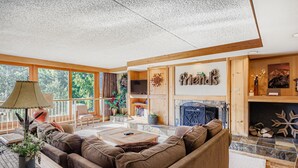 Ein gemütliches Wohnzimmer mit Kamin, Holzbalken und einem großen Fenster mit Blick auf Grünflächen.