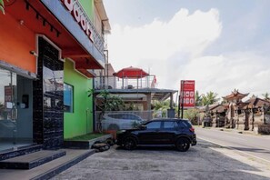 Un edificio con fachada verde, un coche negro estacionado adelante y un letrero rojo al fondo.