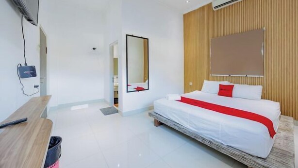 A modern hotel room with a bed, a wooden panel wall, a mounted TV, and a desk. - RedDoorz near Ubud Village (Bali)