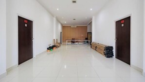 A spacious hallway with white walls and a tiled floor, leading to a room with a wooden panel wall and a bed. - RedDoorz near Ubud Village (Bali)