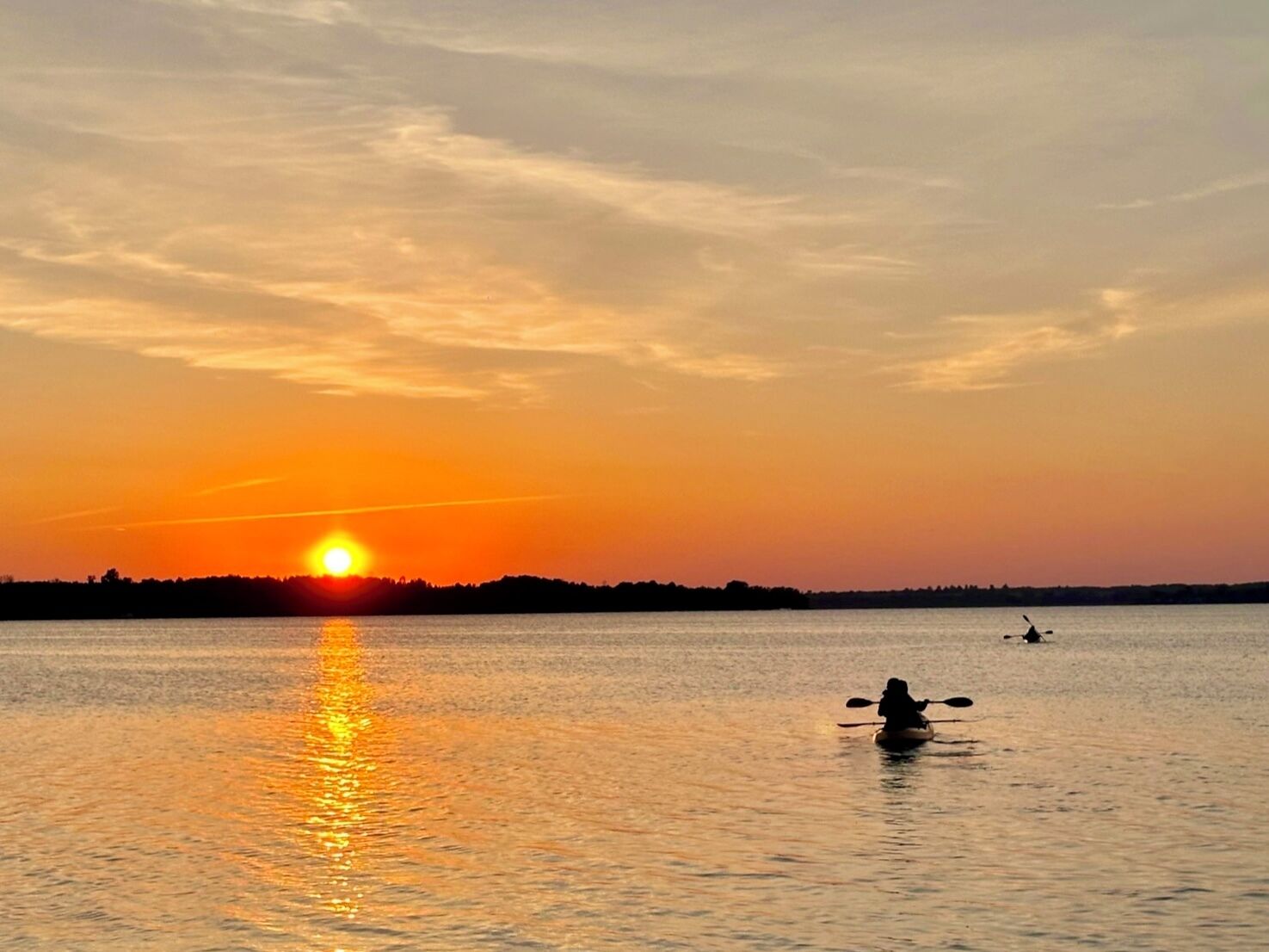 Un coucher de soleil sur une étendue d’eau calme, avec la silhouette d’une personne pratiquant le kayak.