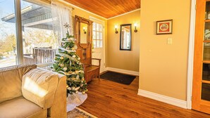 Una sala de estar acogedora con un árbol de Navidad, suelo de madera, un sofá color beige y una puerta que da a otra habitación.